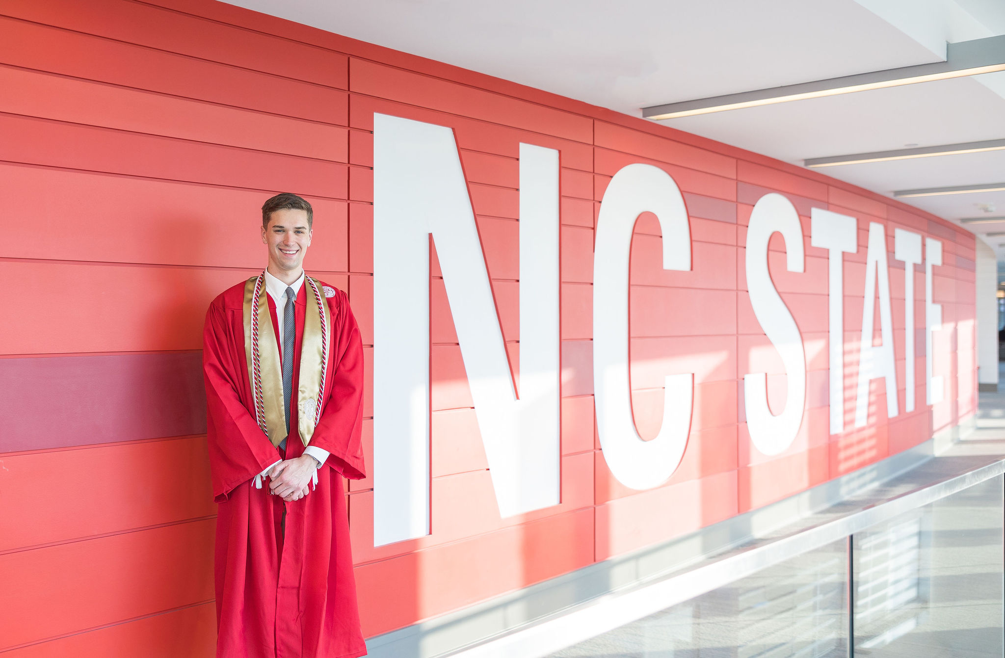 Male grad at ncsu standing in front of red wall