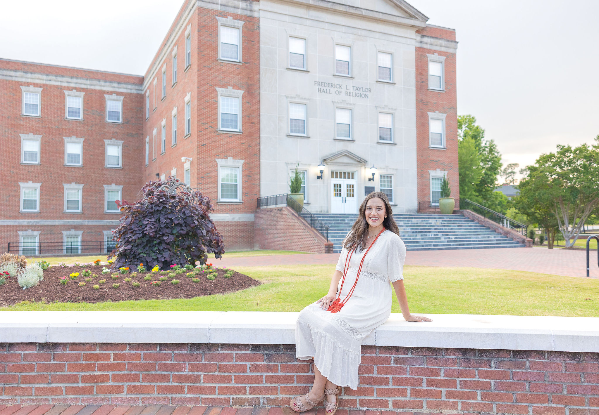 Campbell Grad Sitting on Brick Wall in Long White Dress