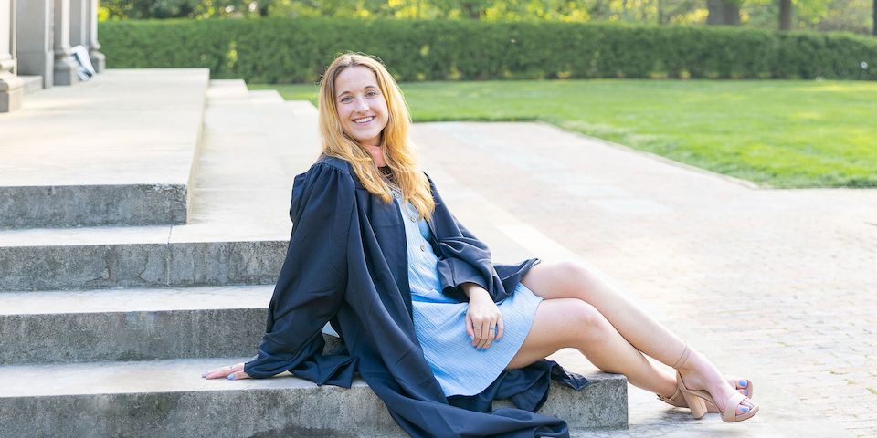 UNC Chapel Hill Grad sitting on steps in cap and gown