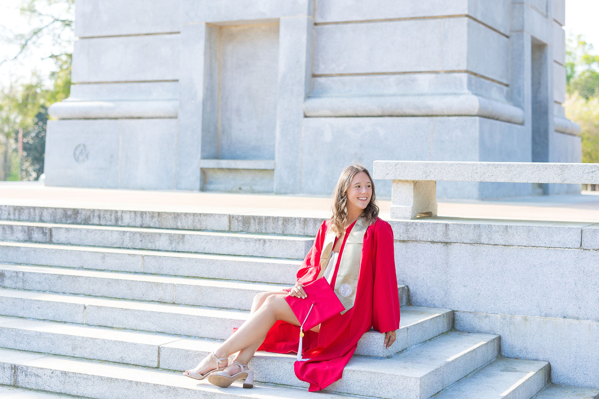 NC State senior sitting on the belltower steps in a red gown and gold stole