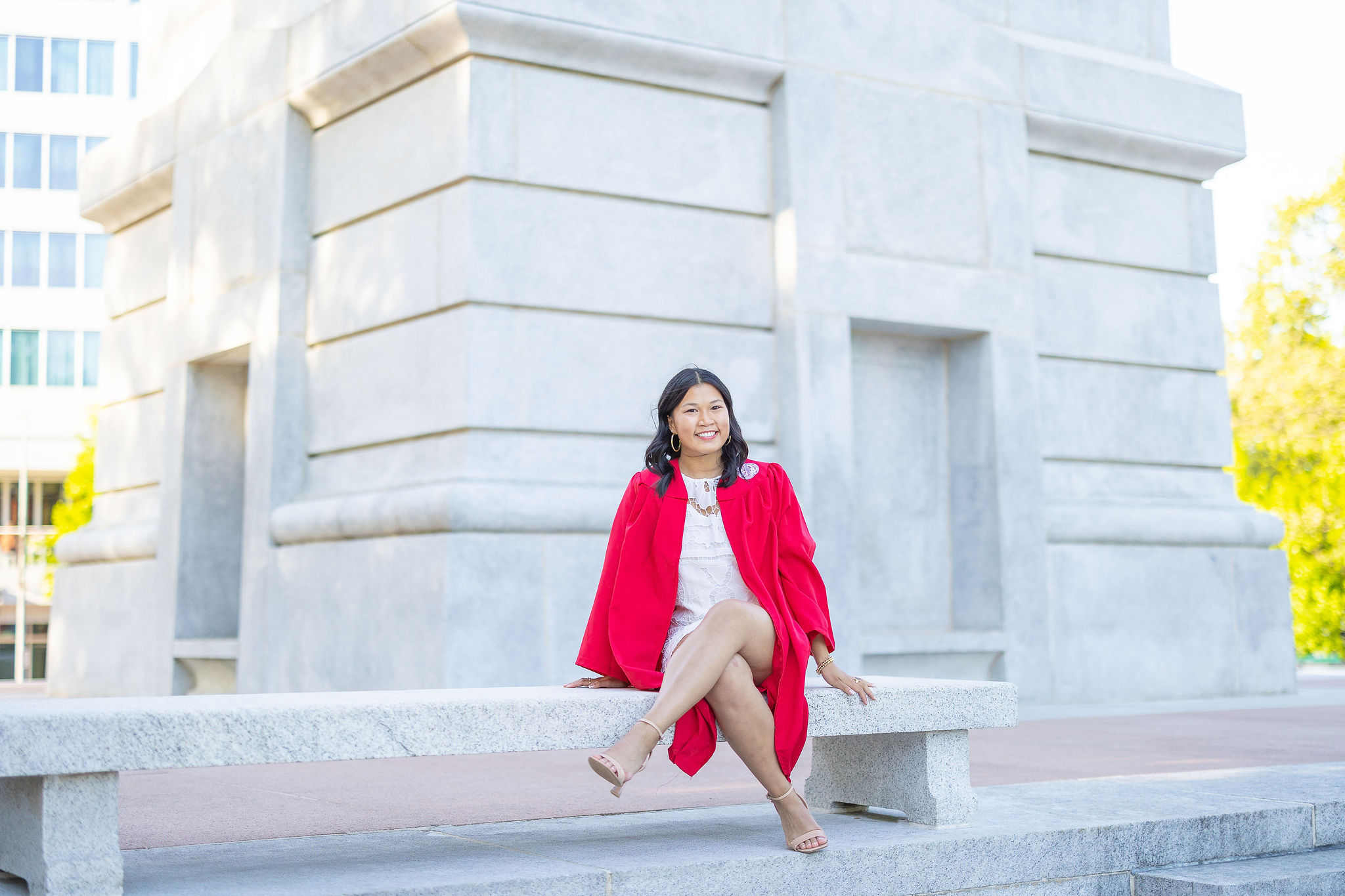 Grad sitting on bench at NC State belltower in red gown