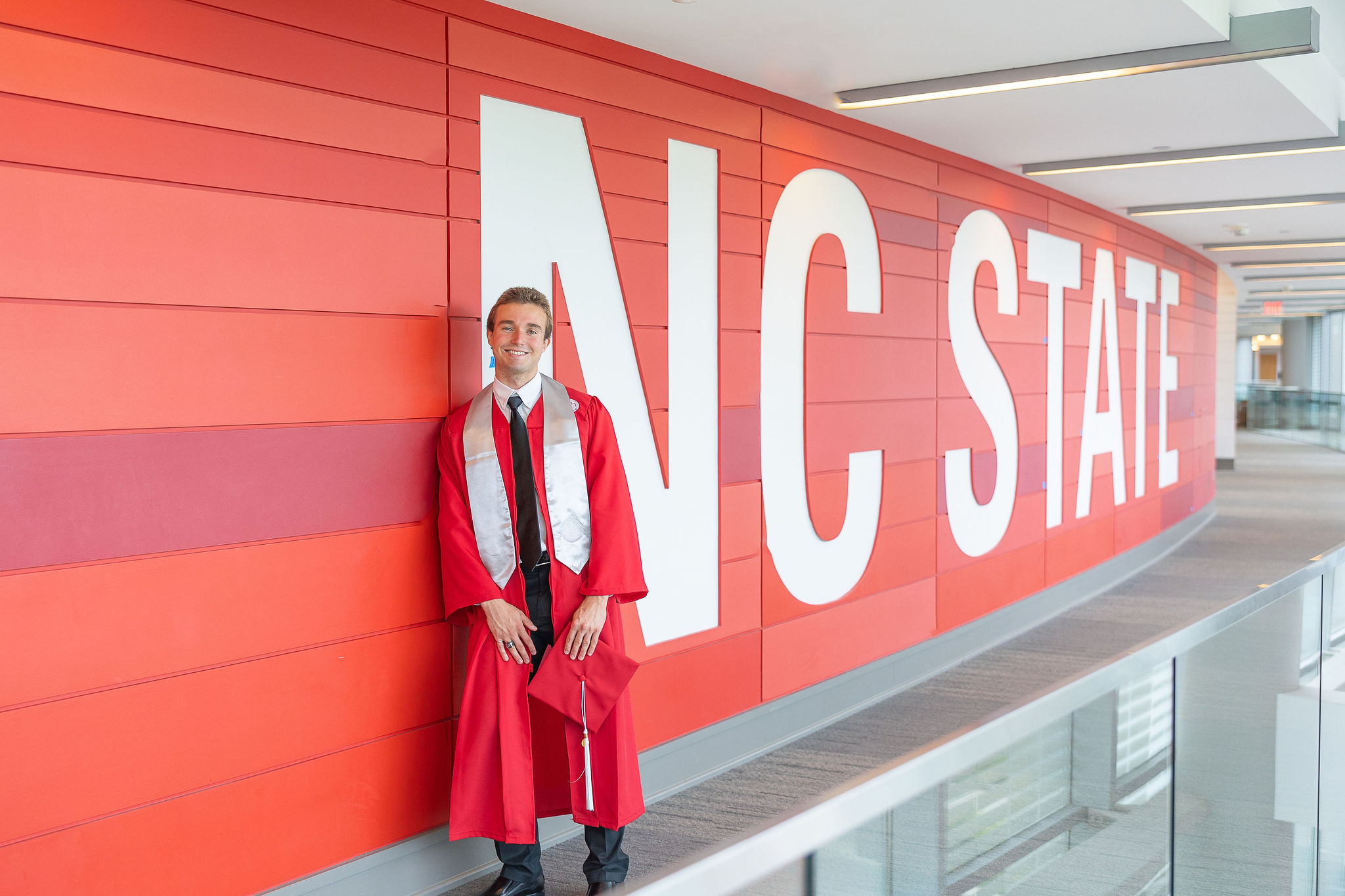 NC State grad standing in front of red wall with white letters that spell out NC State