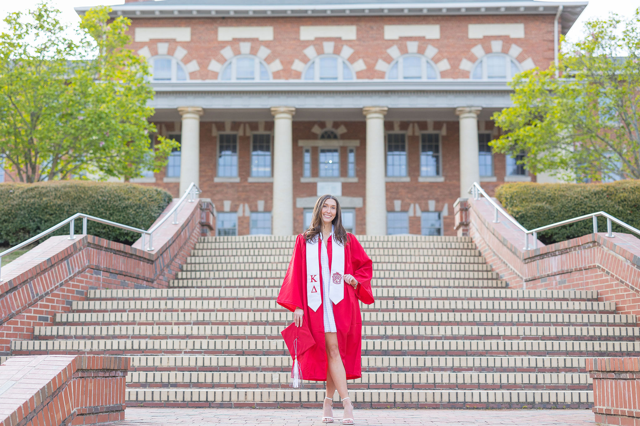 NC State grad in red gown on brick steps