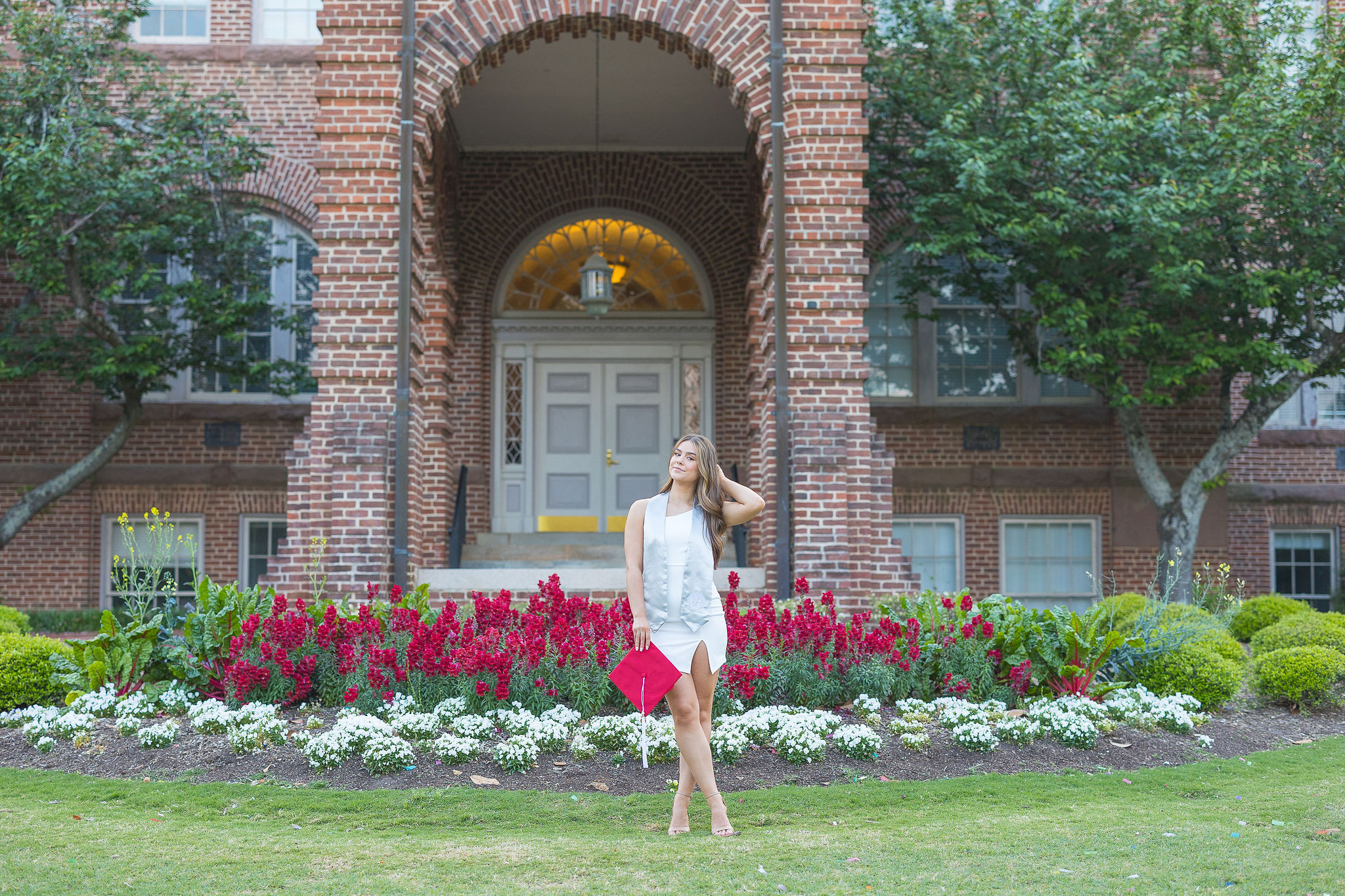 girl in a white dress in field of red flowers posing in front of a brick building