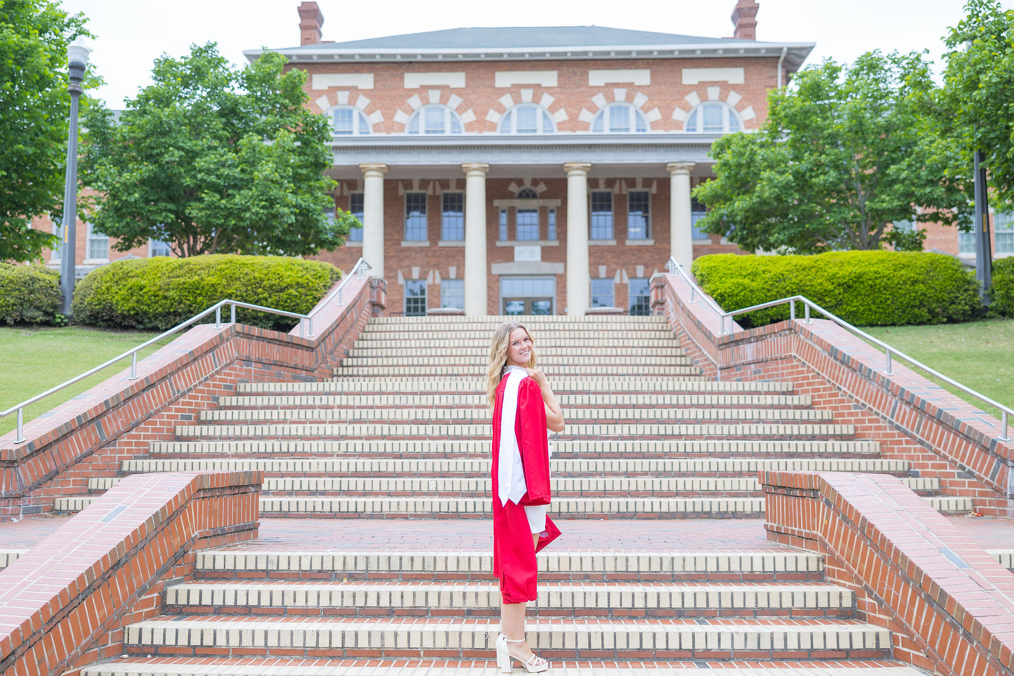 College grad in red gown standing on the brick court of Carolina with stole over the shoulder