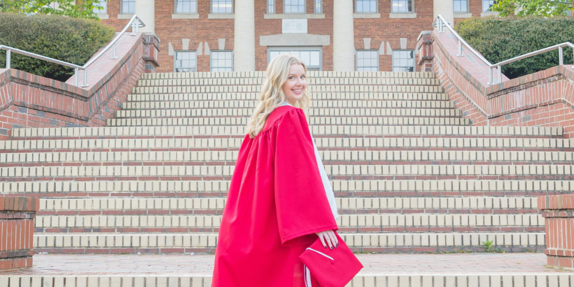 NC State grad in red gown on the steps of the Court of Carolina looking back