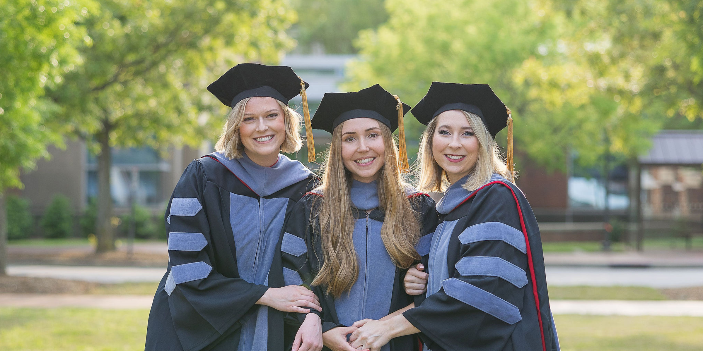 Three friends in grad school caps and gowns outside