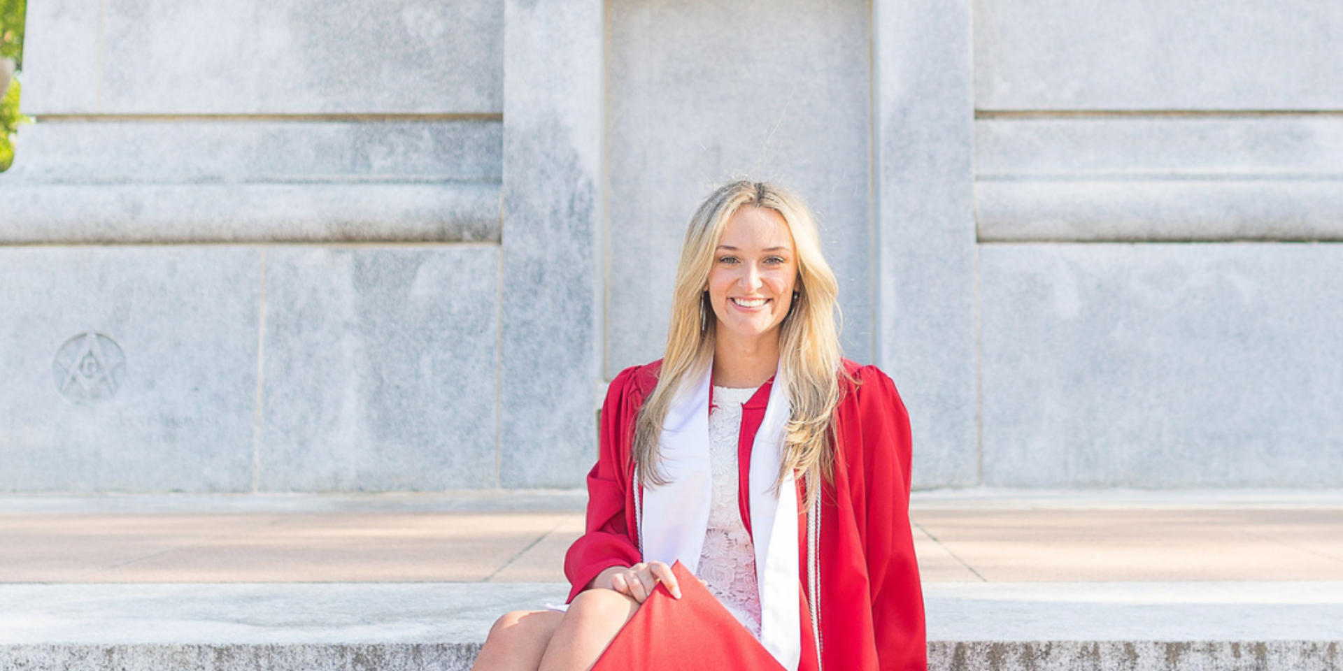 Girl sitting on the steps of the Nc State Belltower in graduation attire