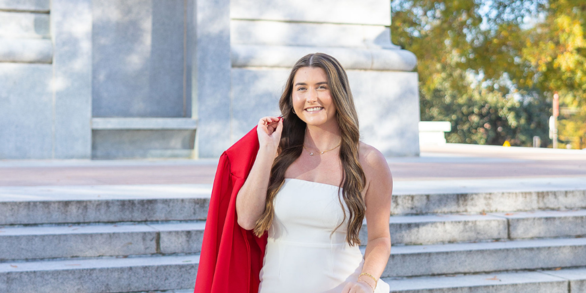 Girl in a white dress holding a red gown over her shoulder