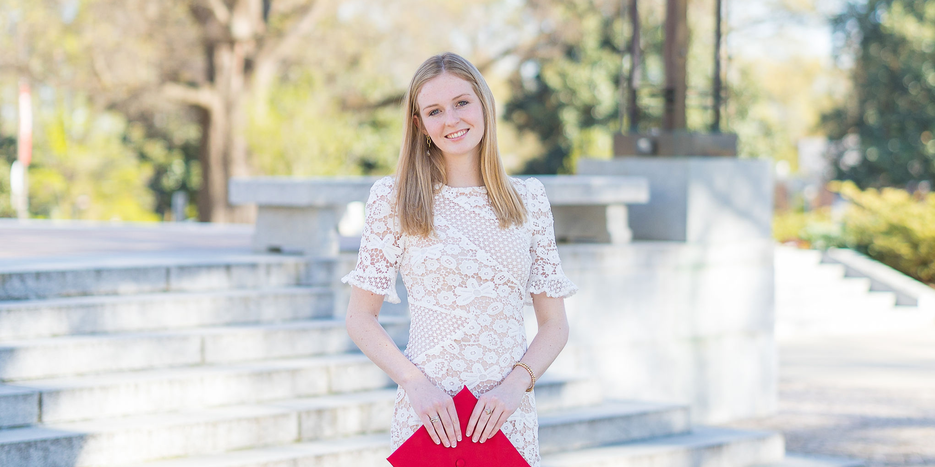 Girl in white lace graduation dress holding a red cap