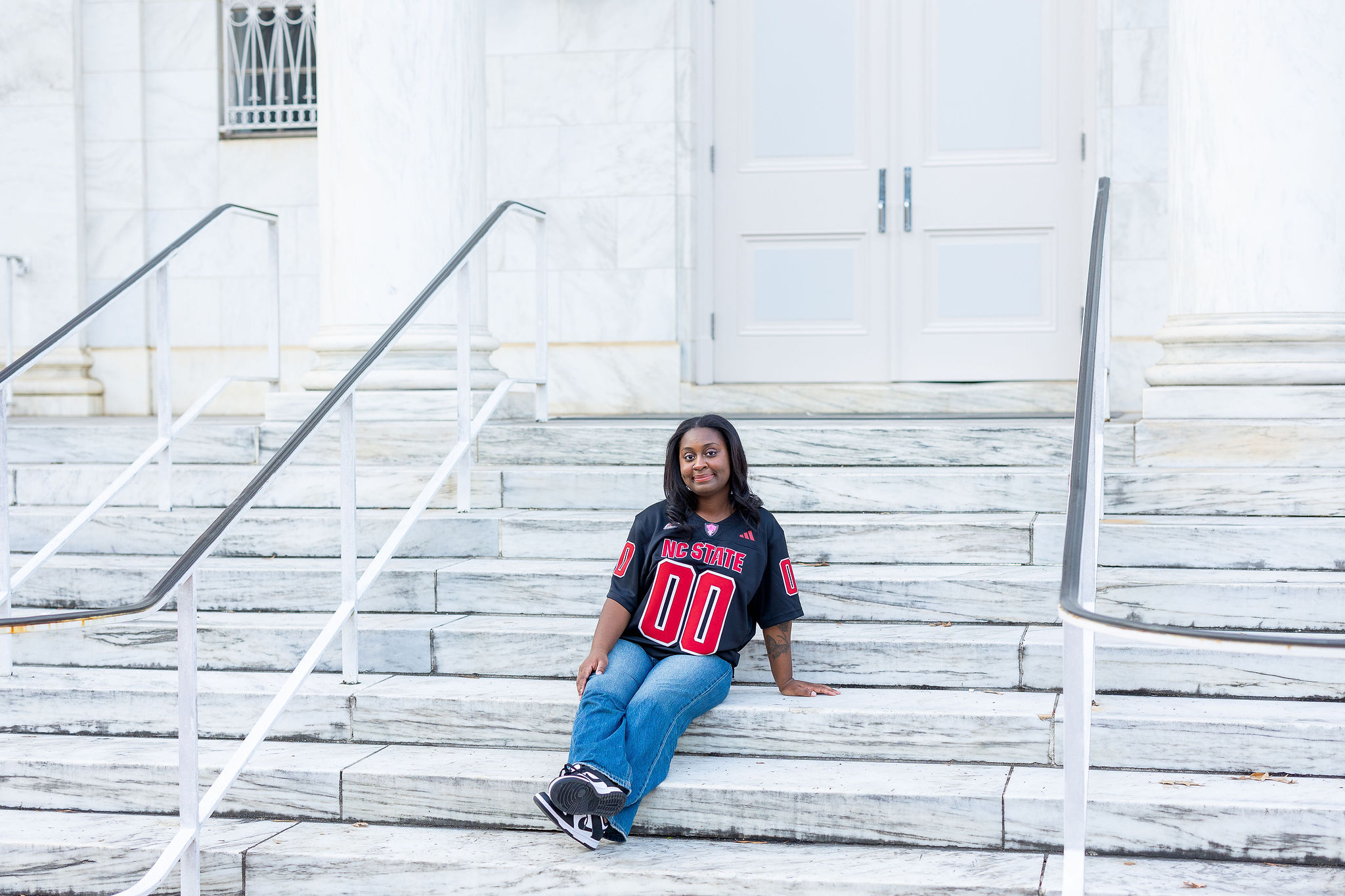 girl sitting on marble steps in an NC State football jersey and jeans