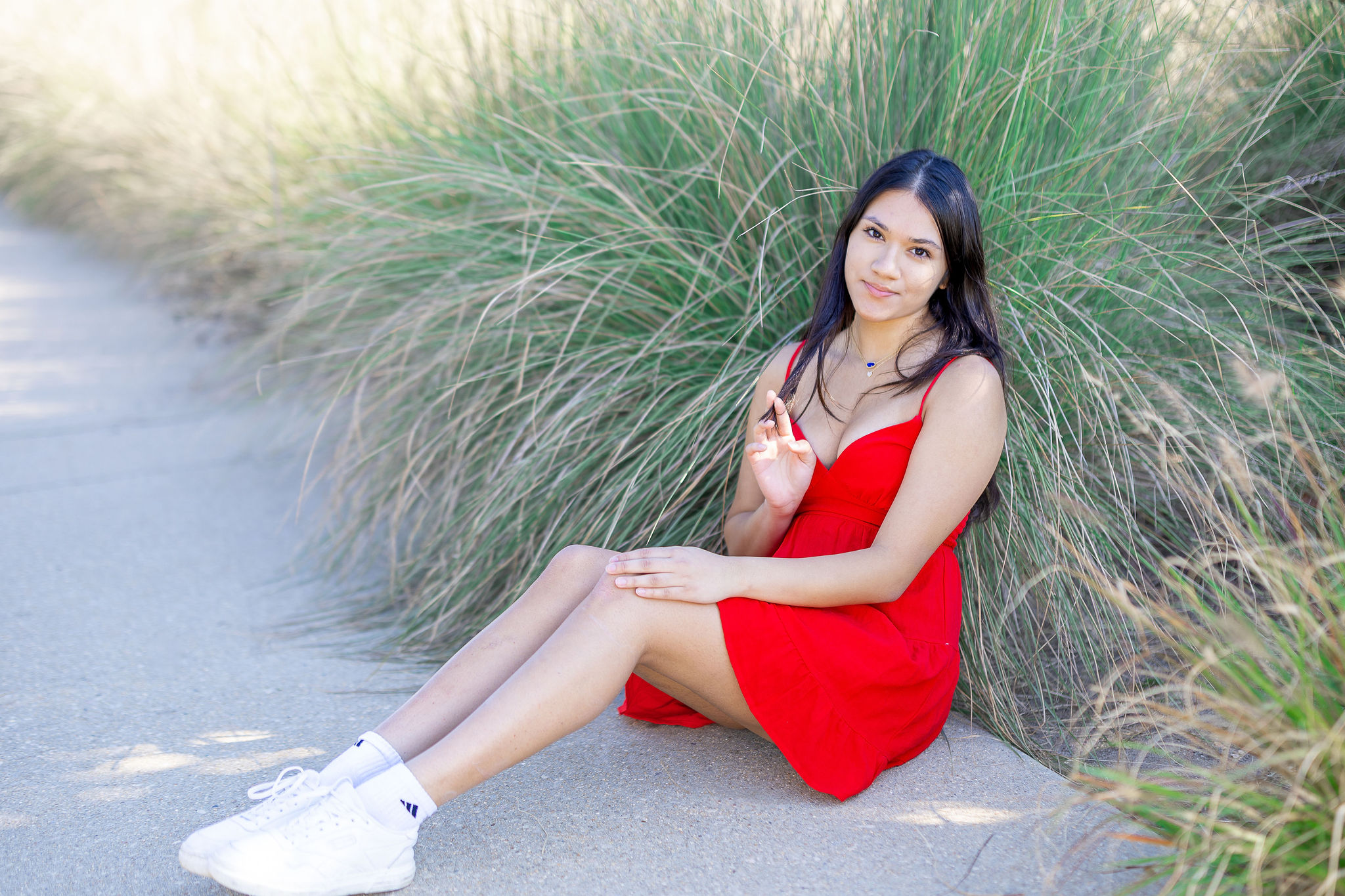 Girl in red dress sitting in front of green grass with white sneakers