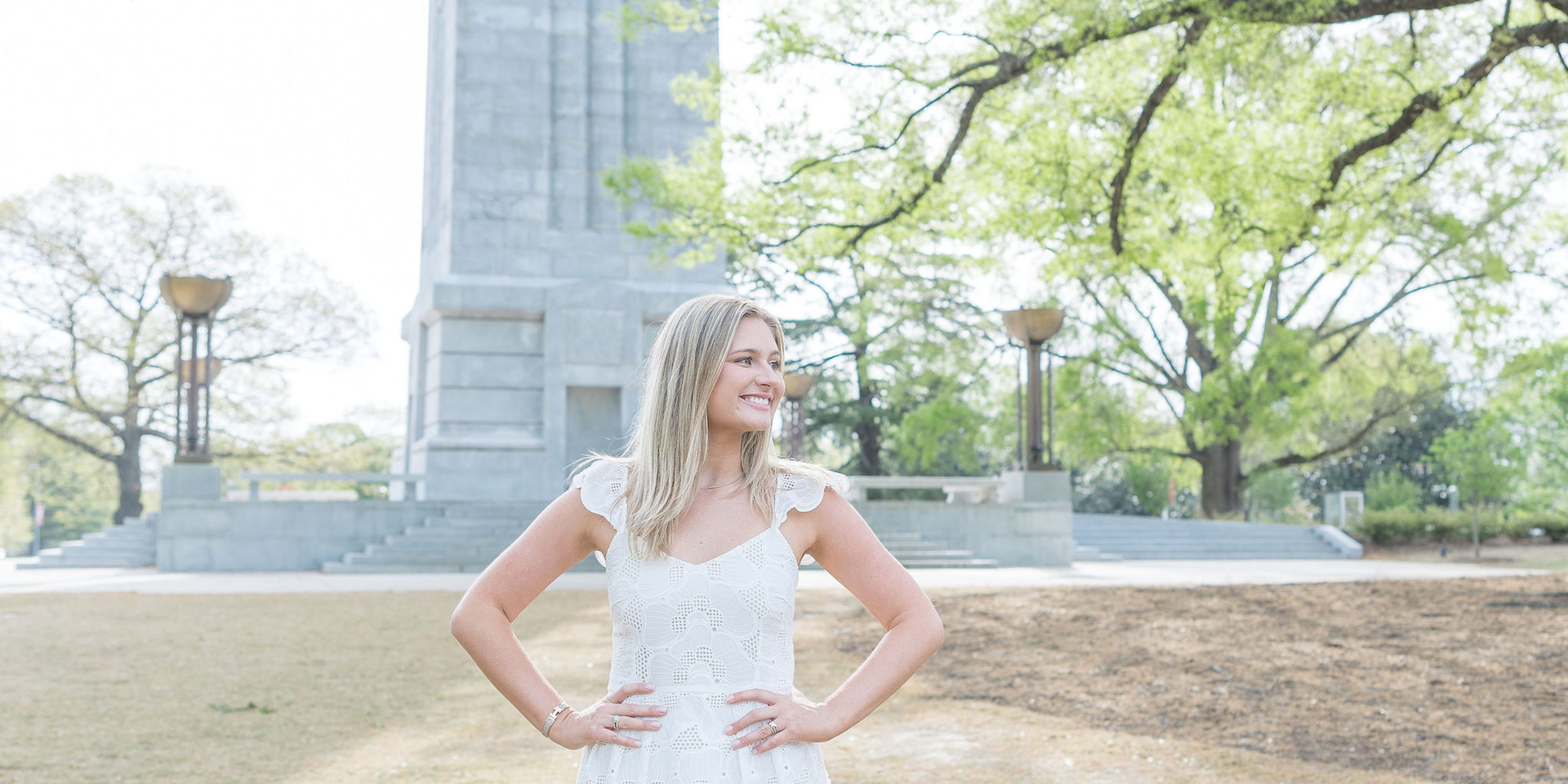 Girl looking to the side in front of the NC State Belltower in a white dress with her hands on her hips