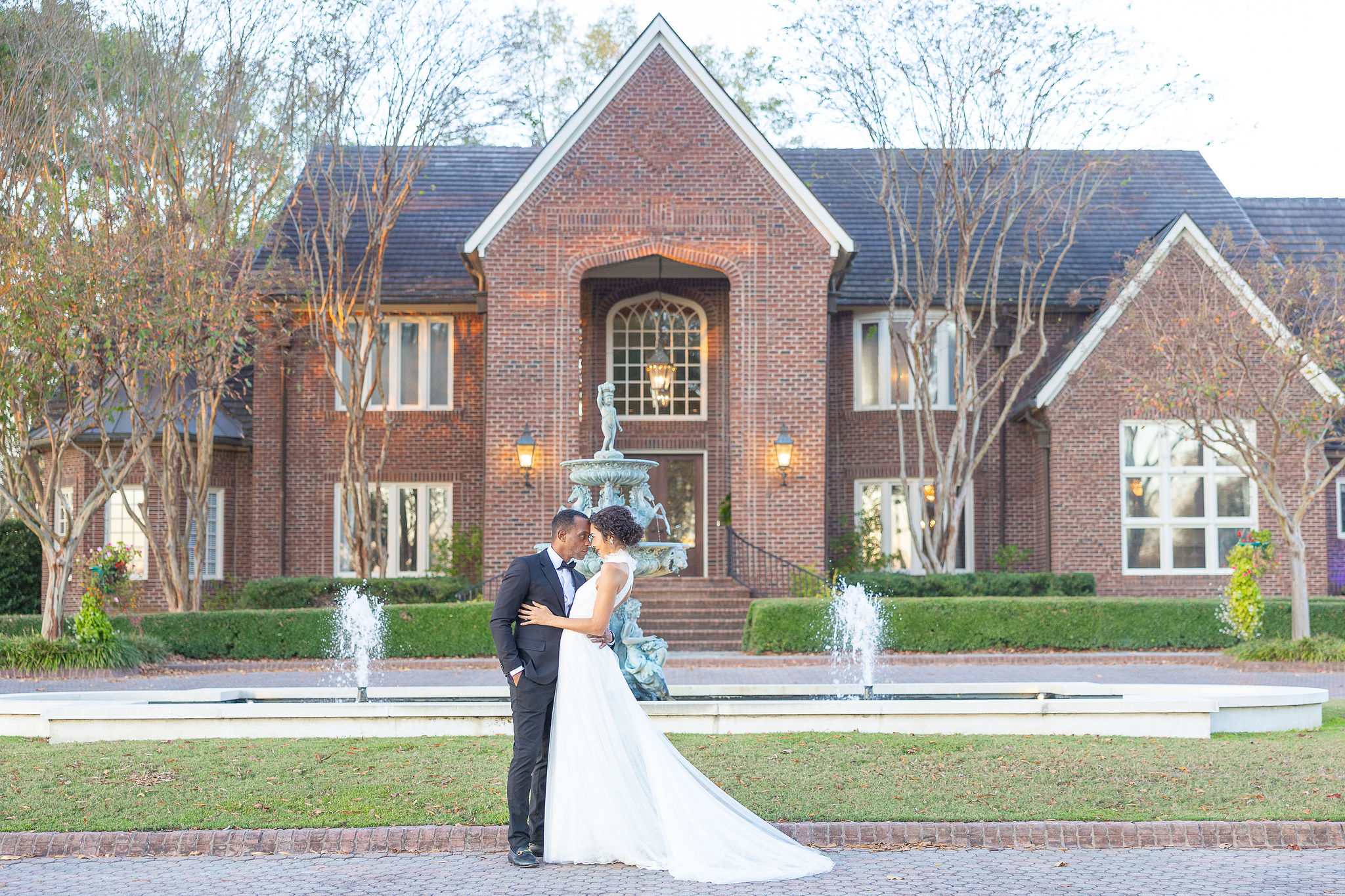 Couple in wedding attire in front of a large red brick house