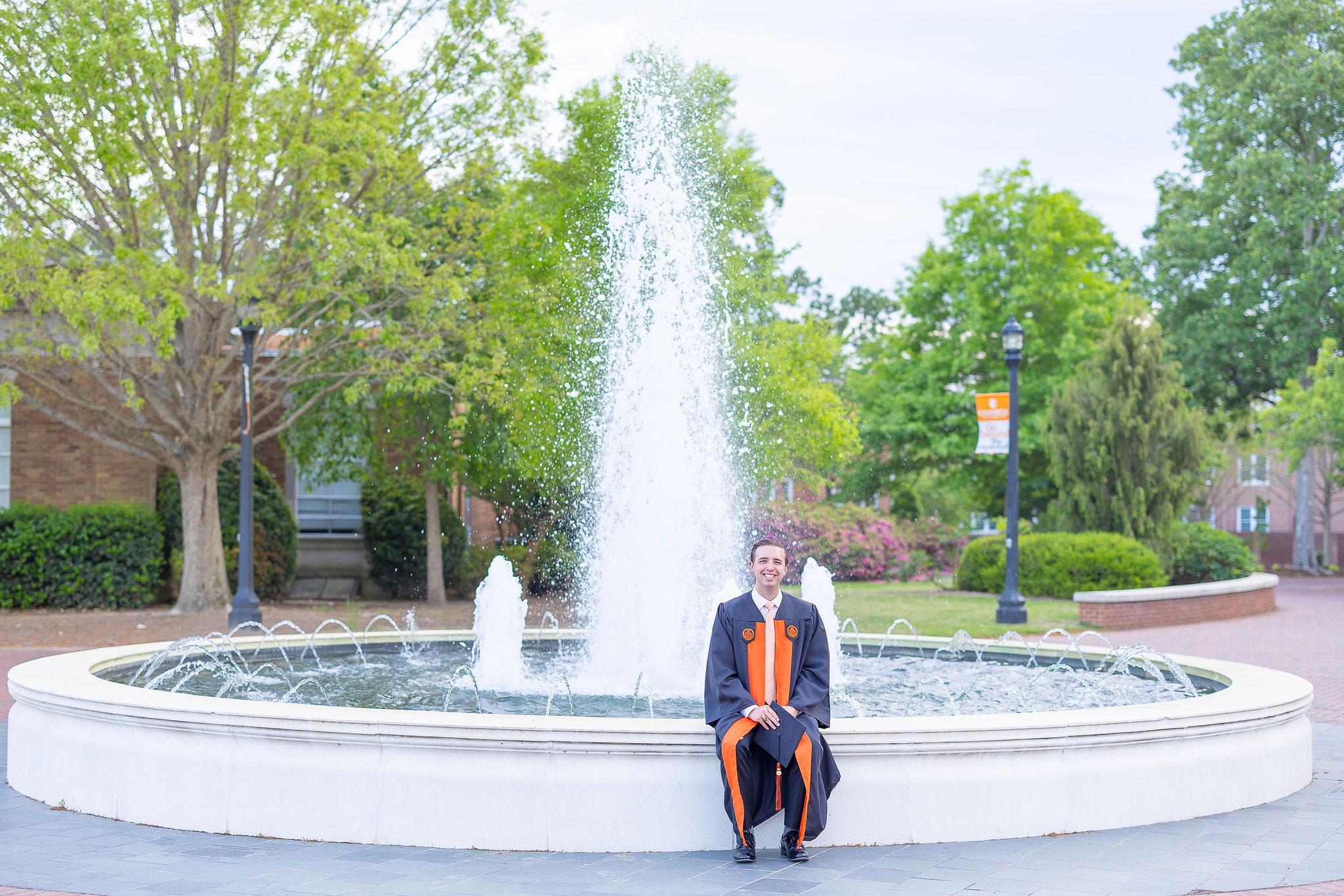 Campbell University graduate in cap and gown sitting in front of a water fountain