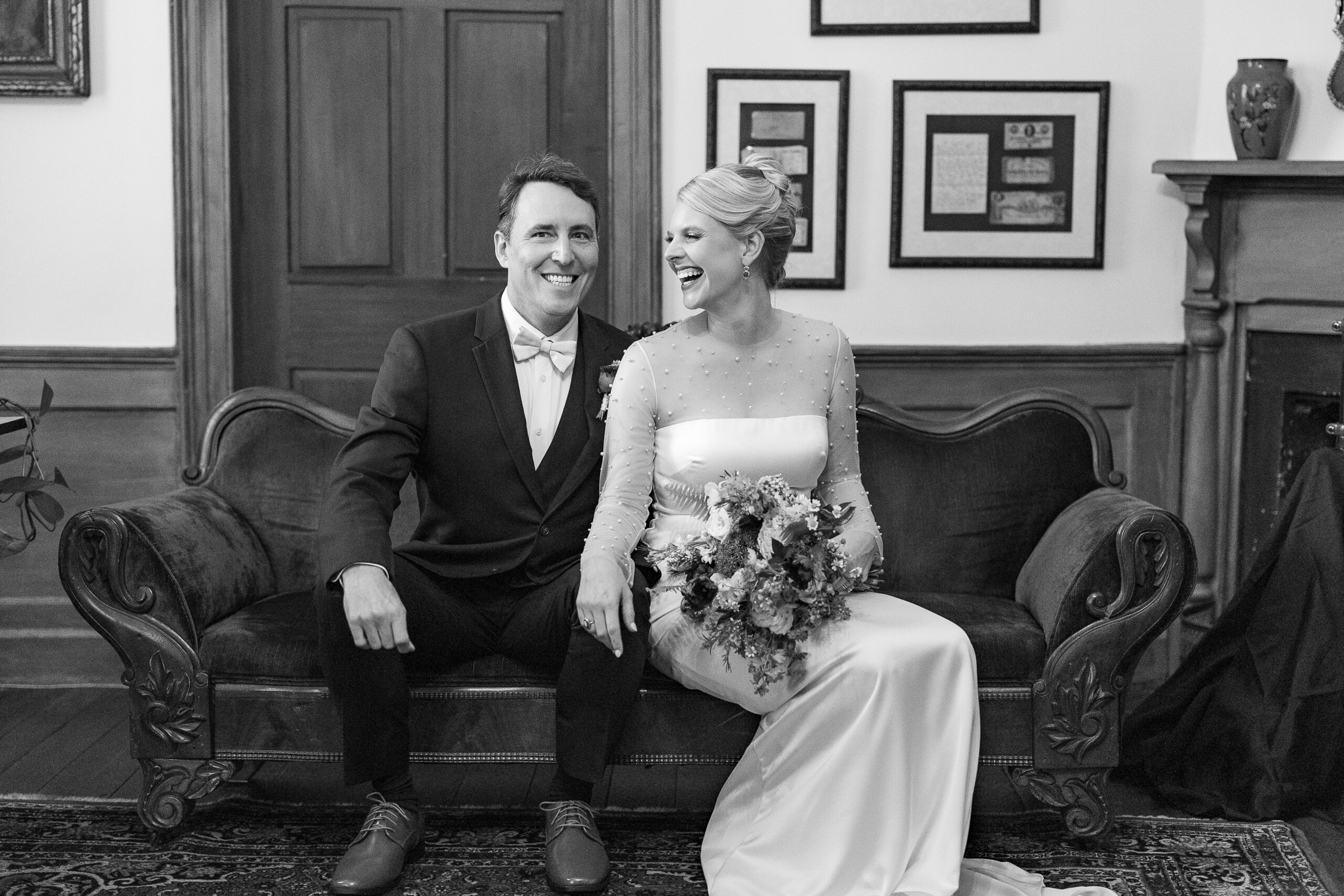 Black and white picture of bride and groom sitting on bench laughing