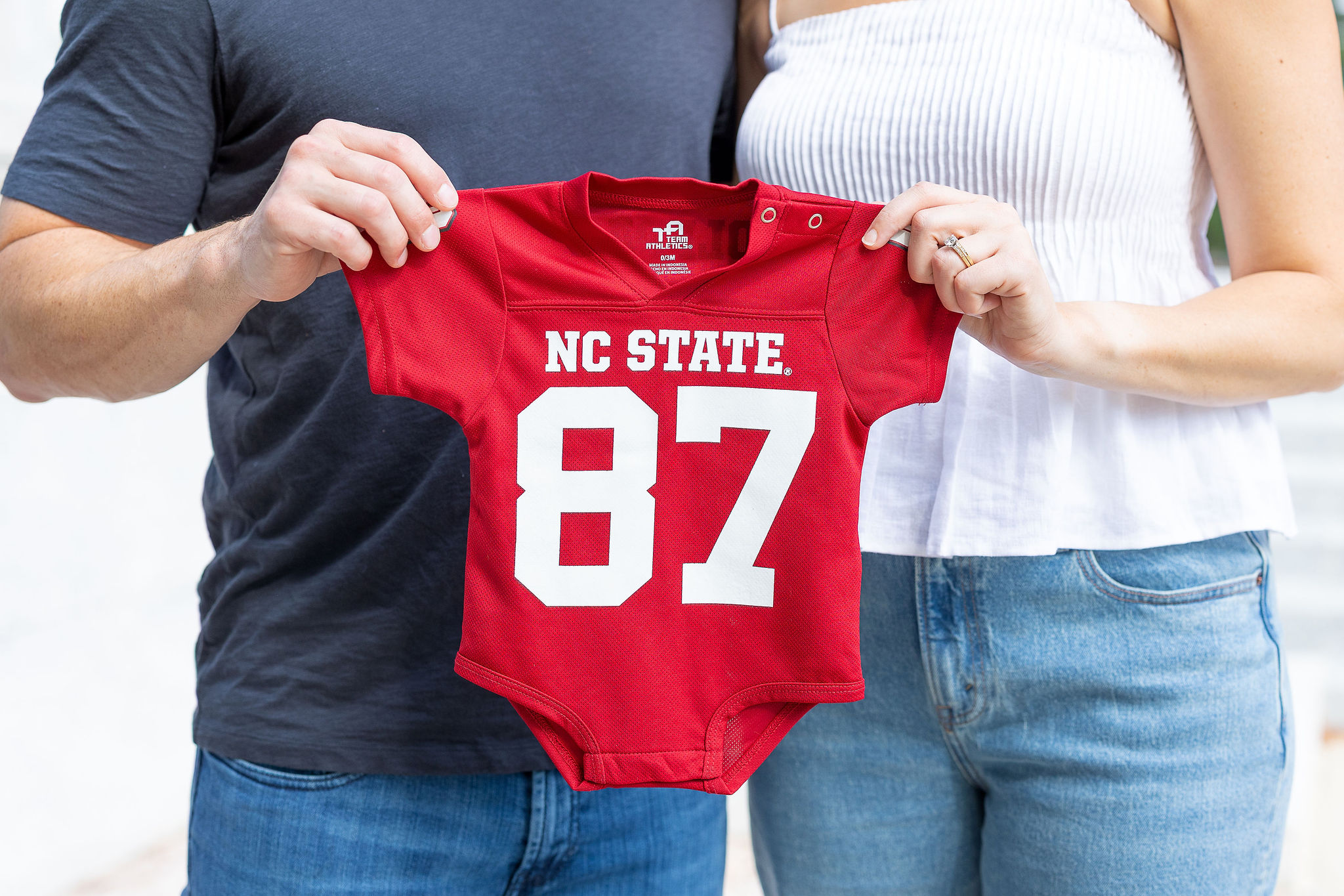 Couple holding NC State baby onsie