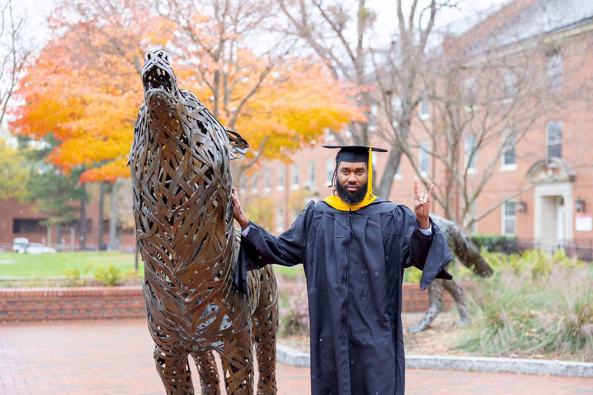 NC State Masters Grad holding up a wolf sign in front of iron wold statue