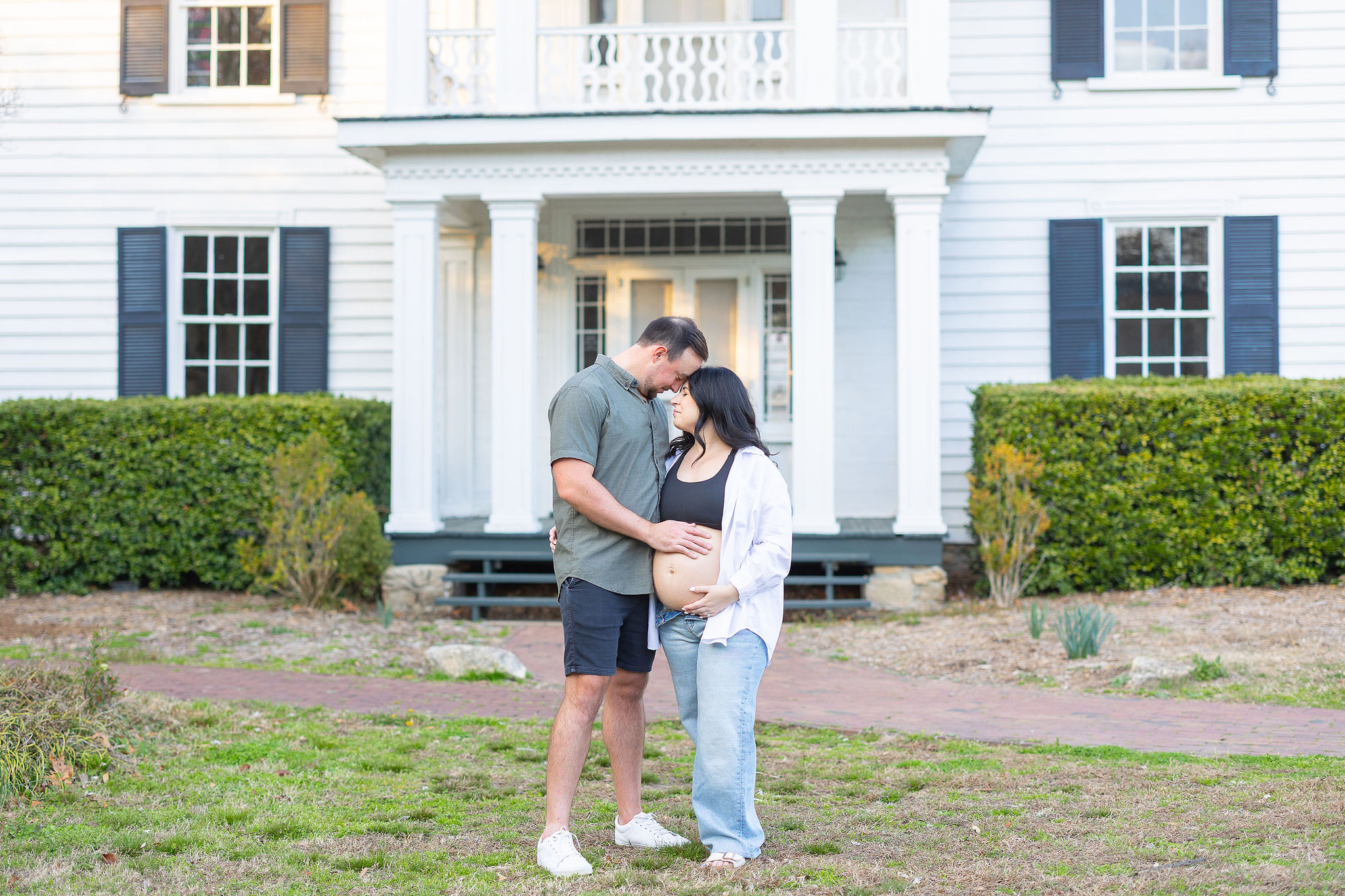 expecting couple in front of white estate style home