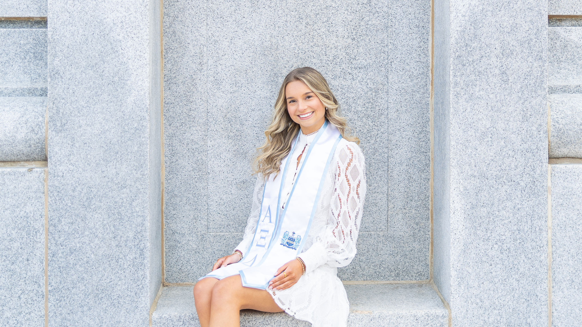 NC State graduate in white lace dress sitting in bell tower cut out