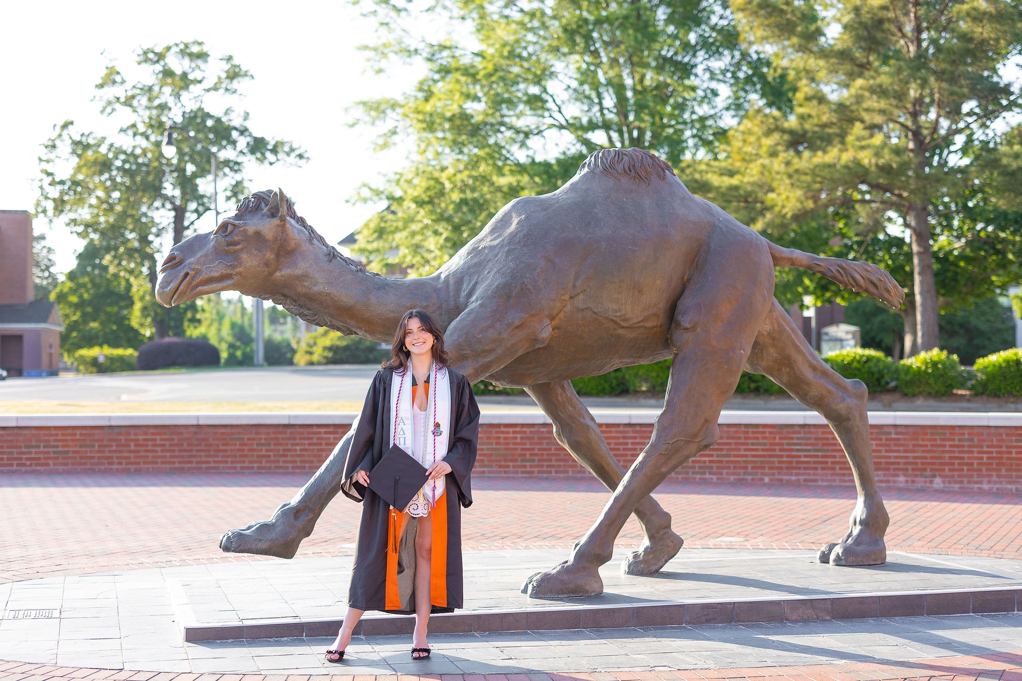 Campbell University graduate standing in front of camel statue in cap and gown