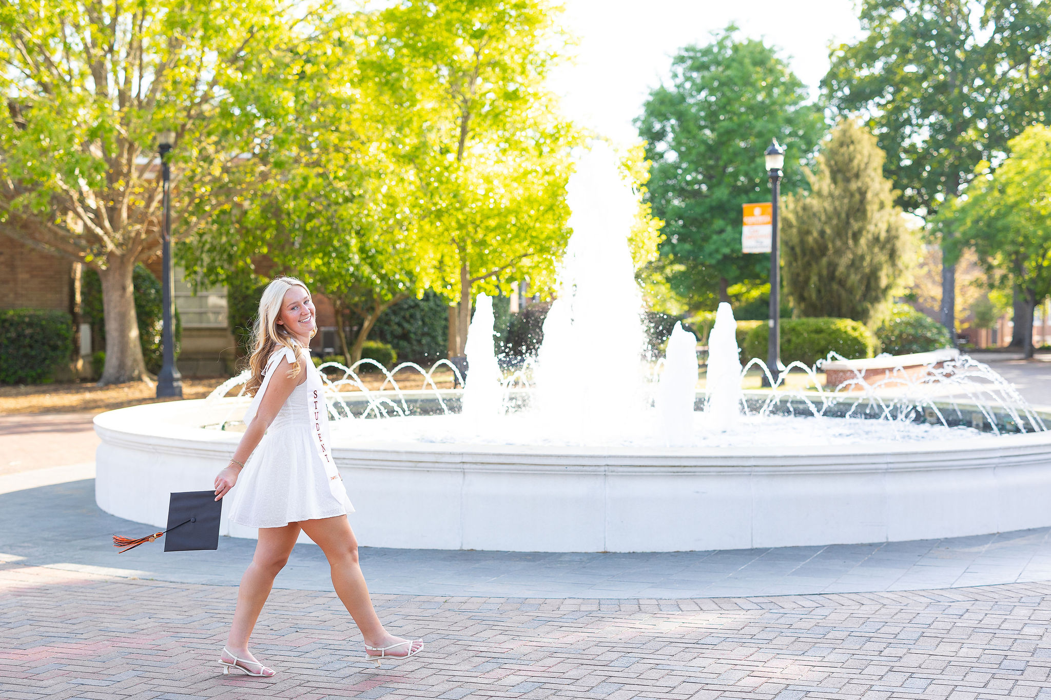 Campbell University grad walking across courtyard in front of fountain