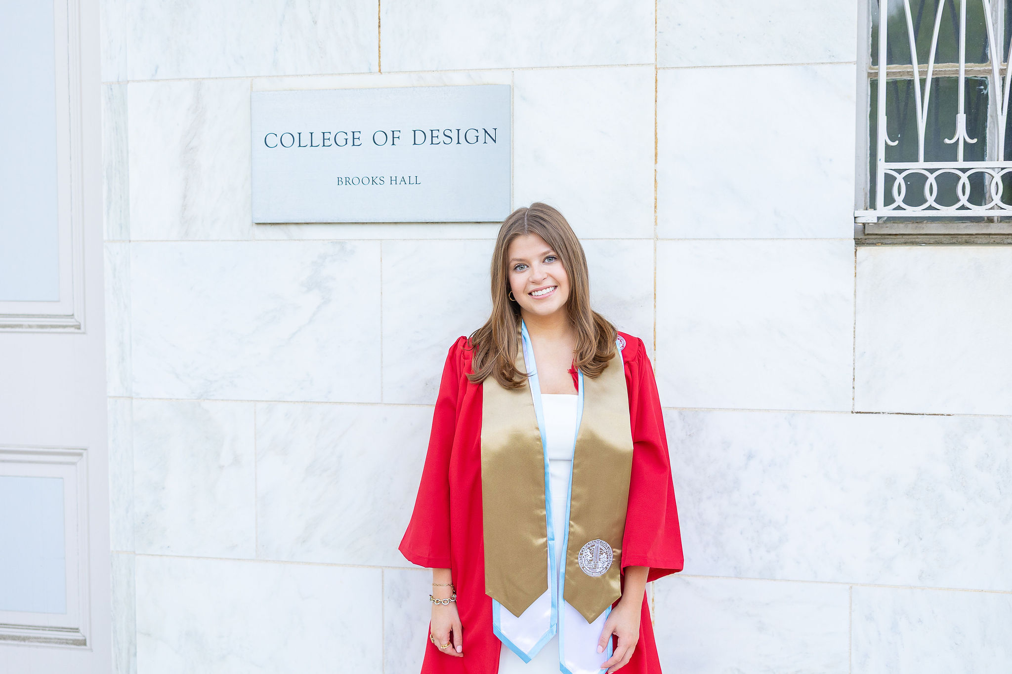 NC State senior in gown in front of the College of Design