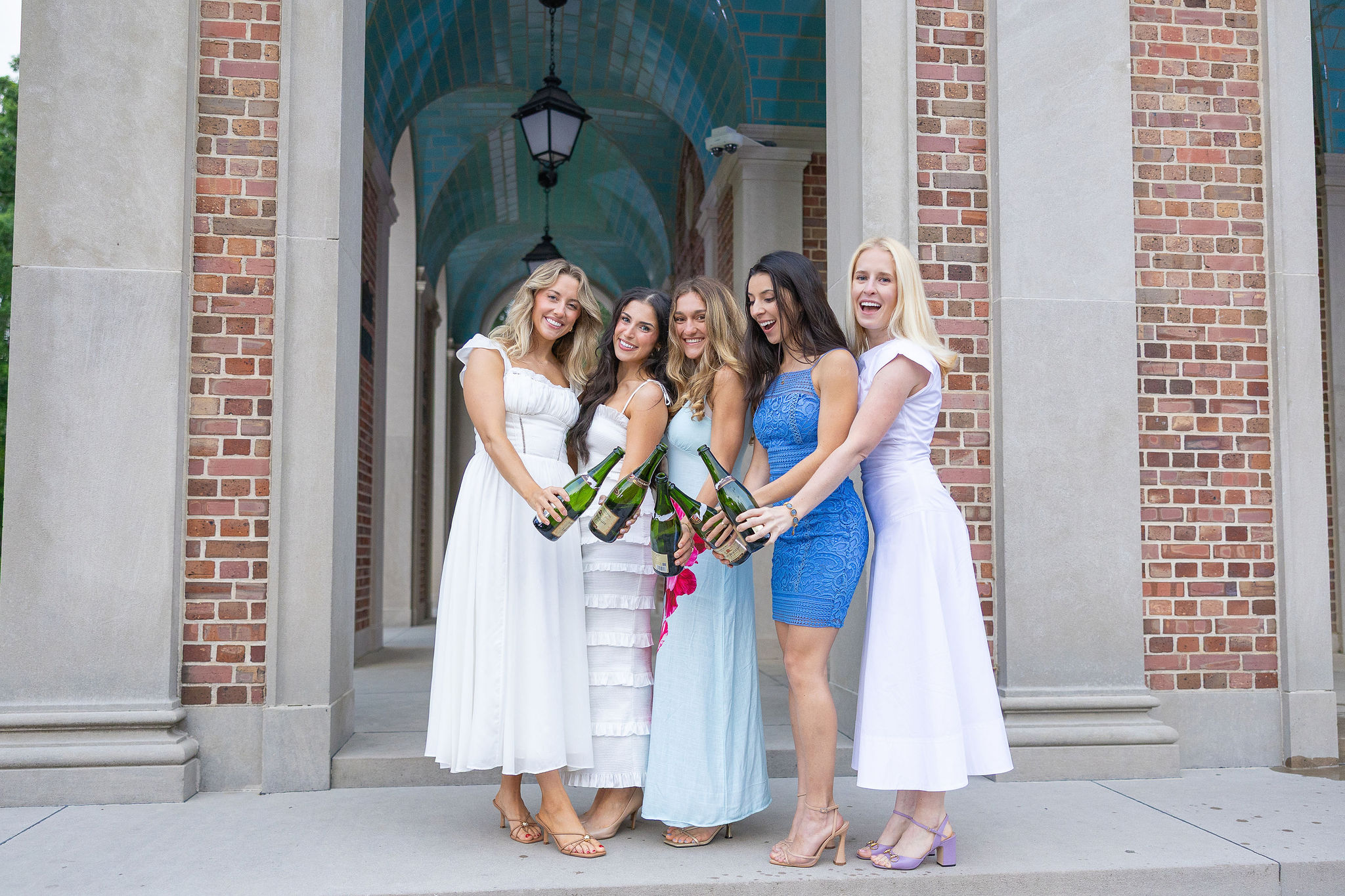 group of girls clinking champagne bottles in colorful dresses on chapel hill campus steps