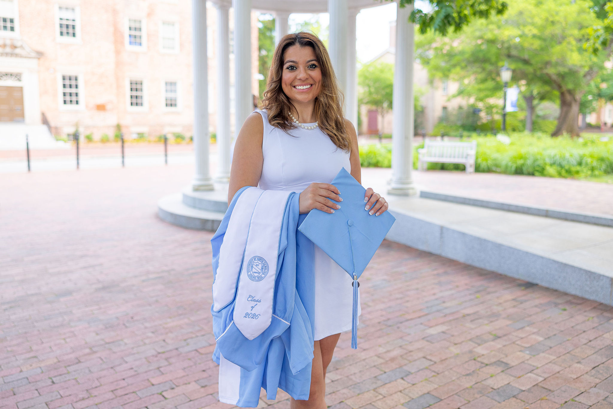 UNC graduate at old well with cap, gown, and stole draped over arm