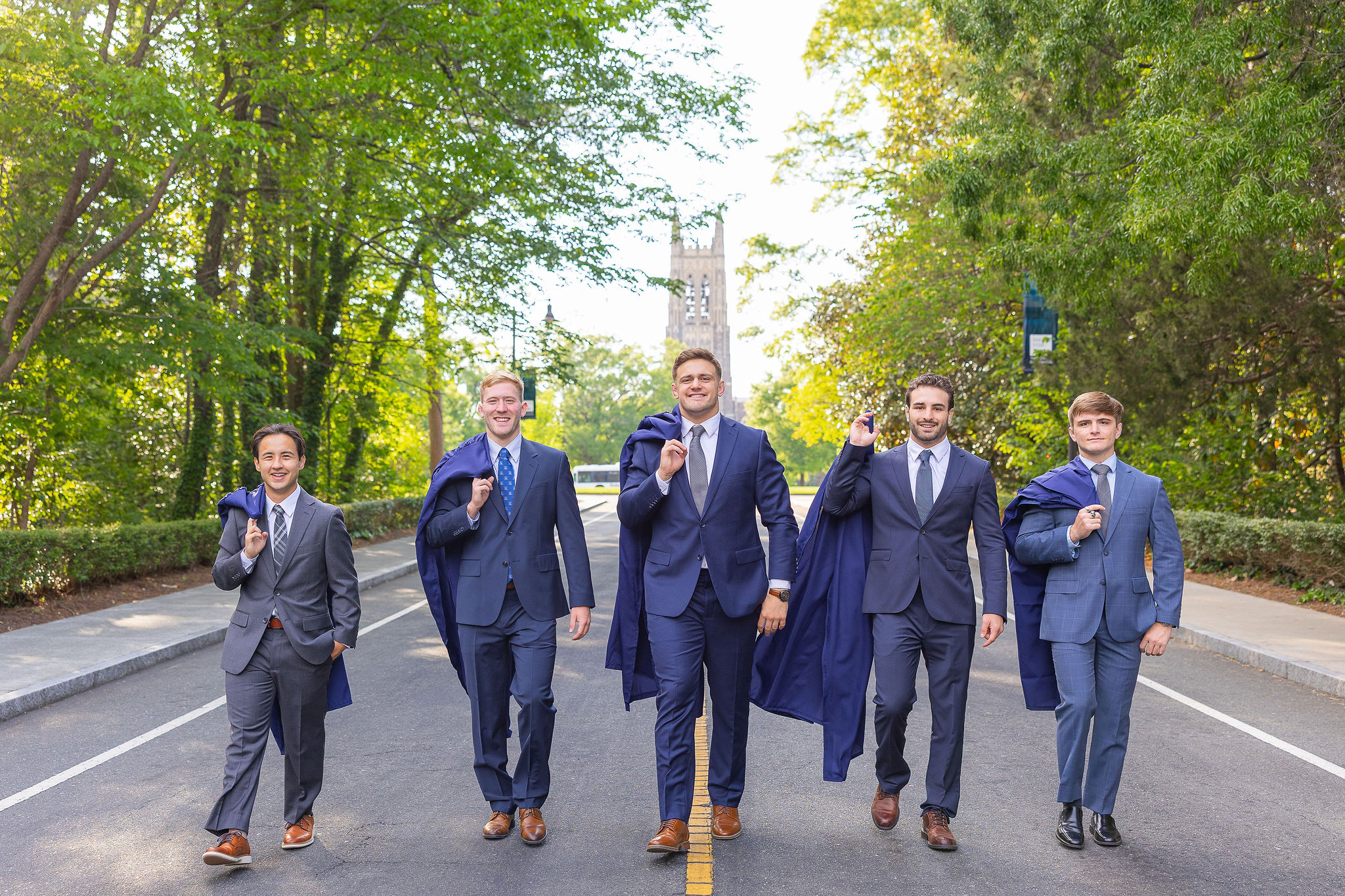 duke grads in suits walking with gown over there shoulder