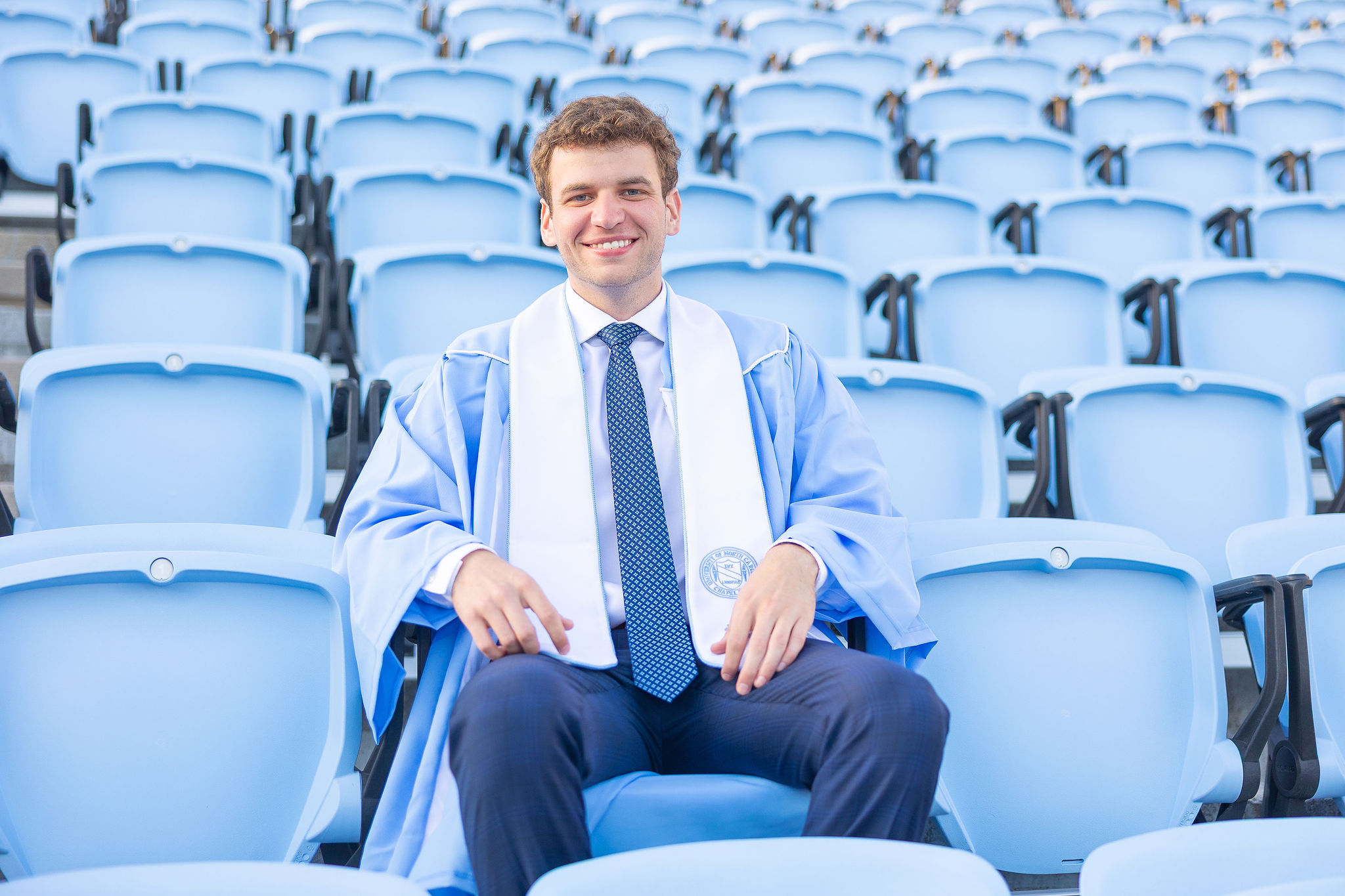 UNC Chapel Hill Senior sitting in football stadium in graduation gown and stole