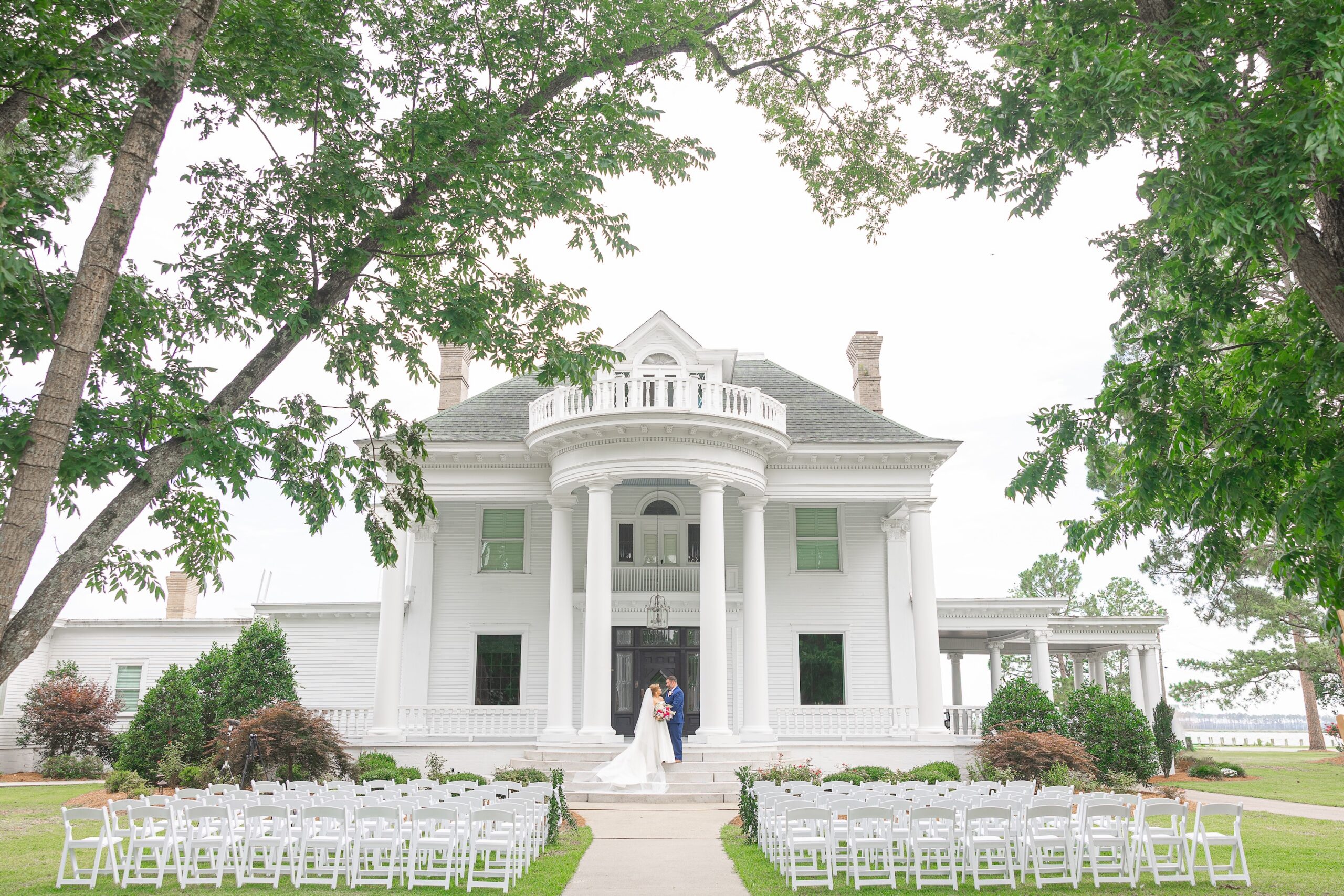 bride and groom in front of estate and lawn covered with white chairs