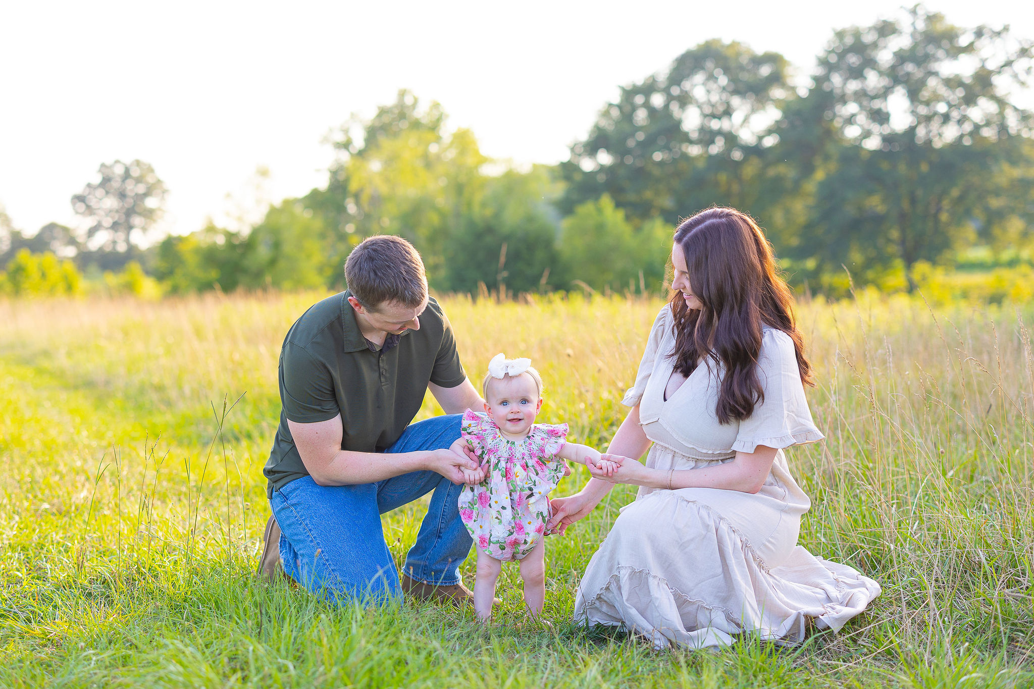 Mom and Dad holding the baby's hands in field