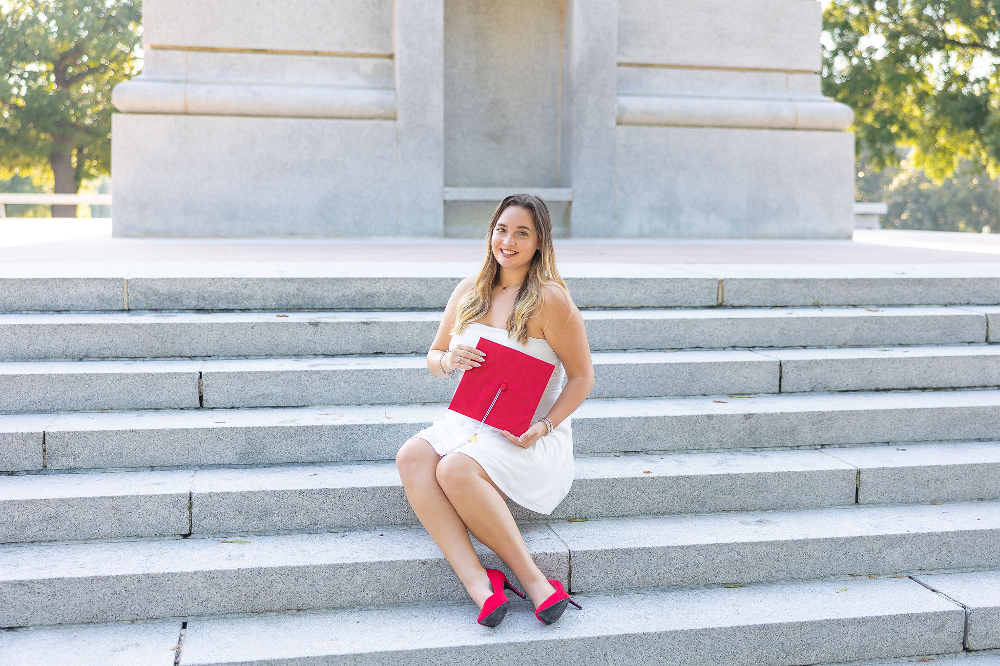 girl sitting on belltower steps holding red graduation cap