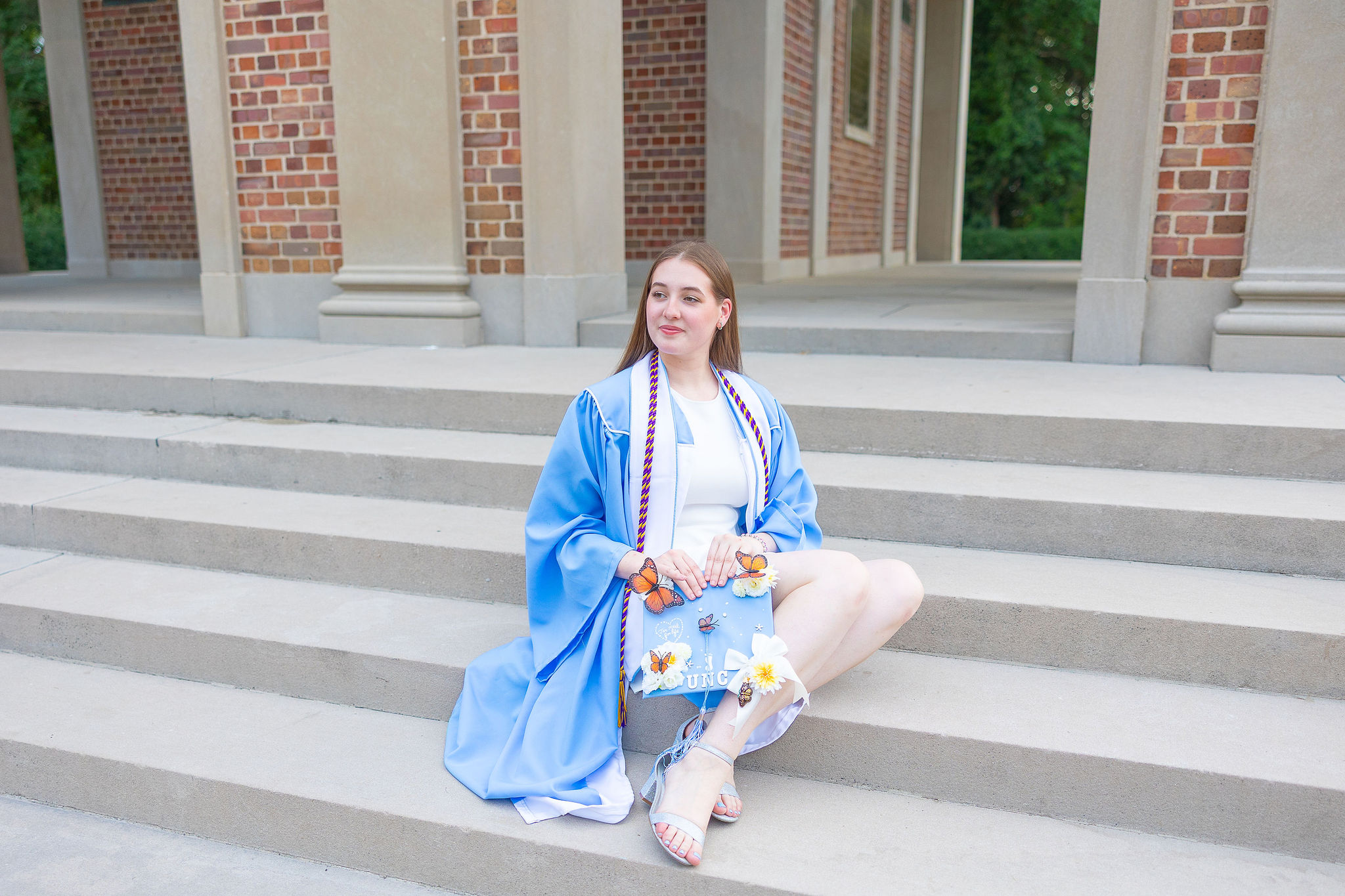 UNC grad sitting on steps in blue graduation gown