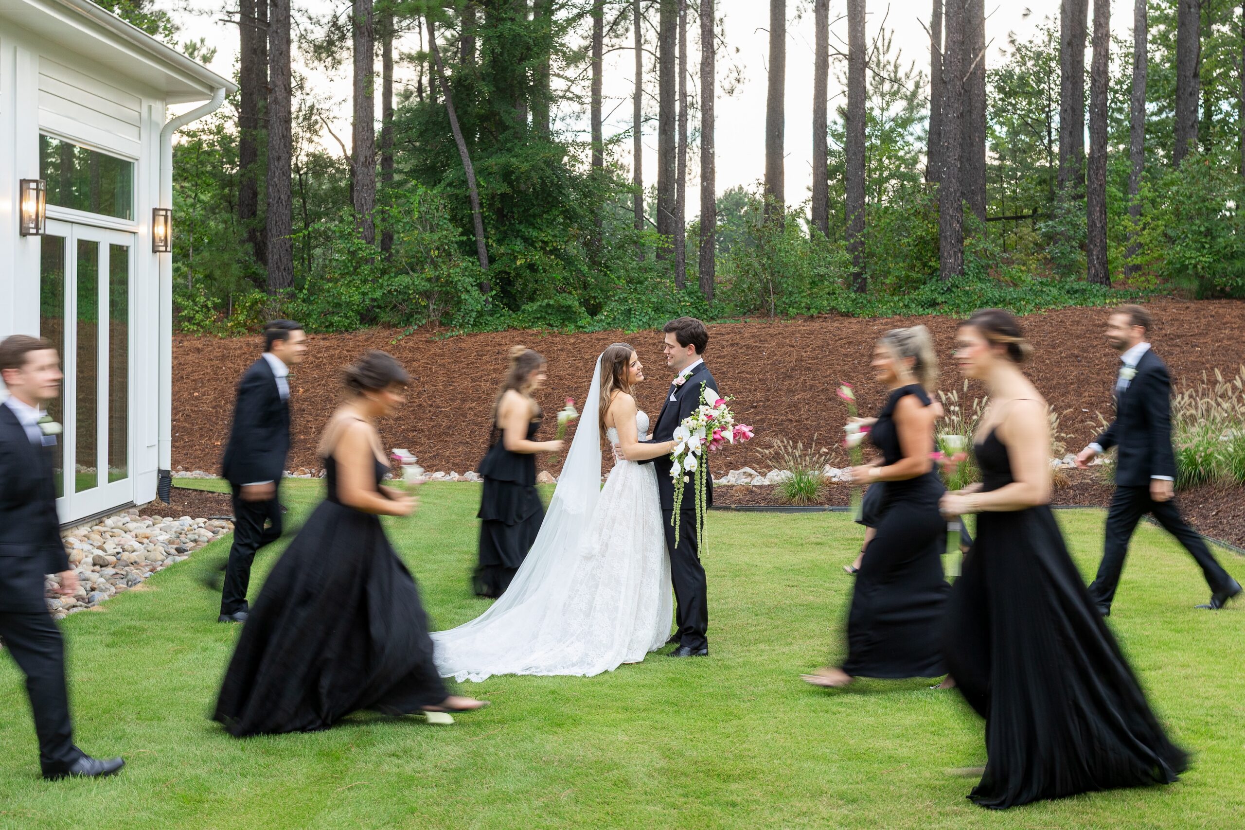 bridal party in black walking around bride and groom in field